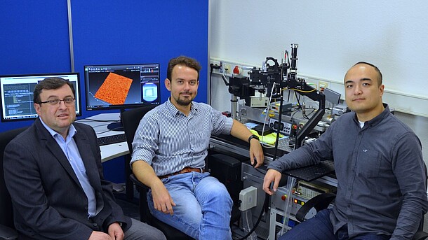 Drei Männer sitzen vor Tischen mit Instrumenten in einem Labor